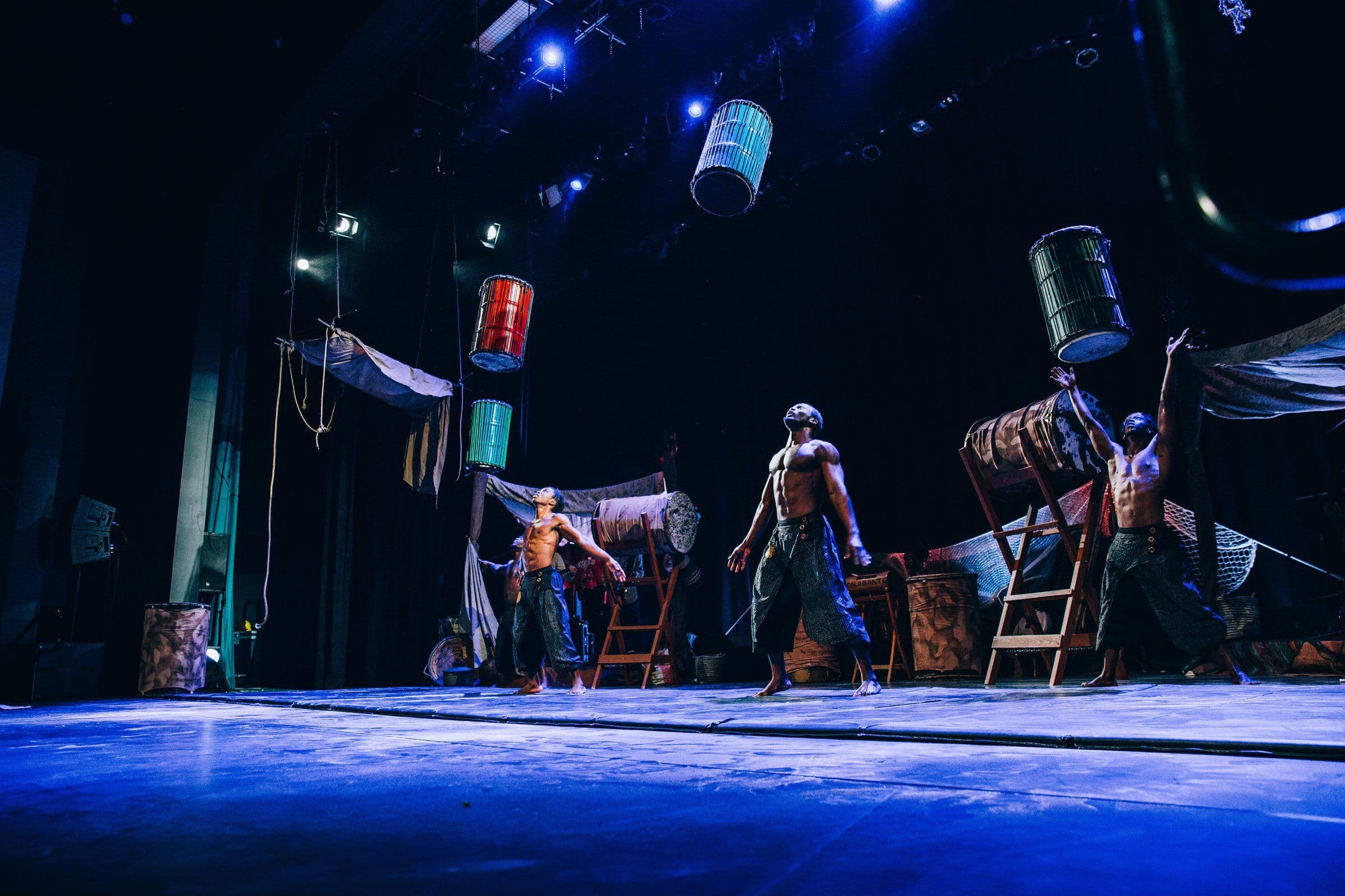 a group of men are performing on a stage with barrels on their shoulders .