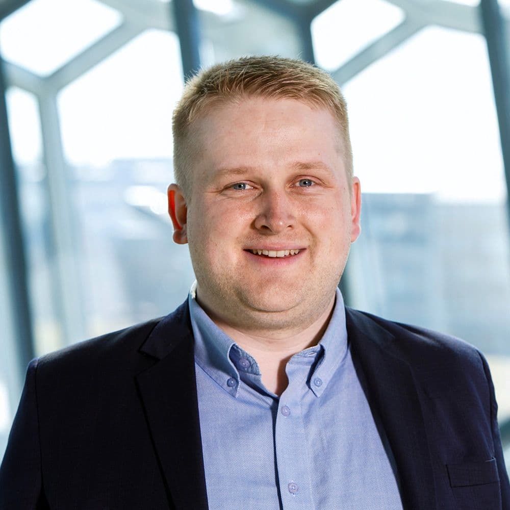 a man in a suit and blue shirt is smiling in front of a window .