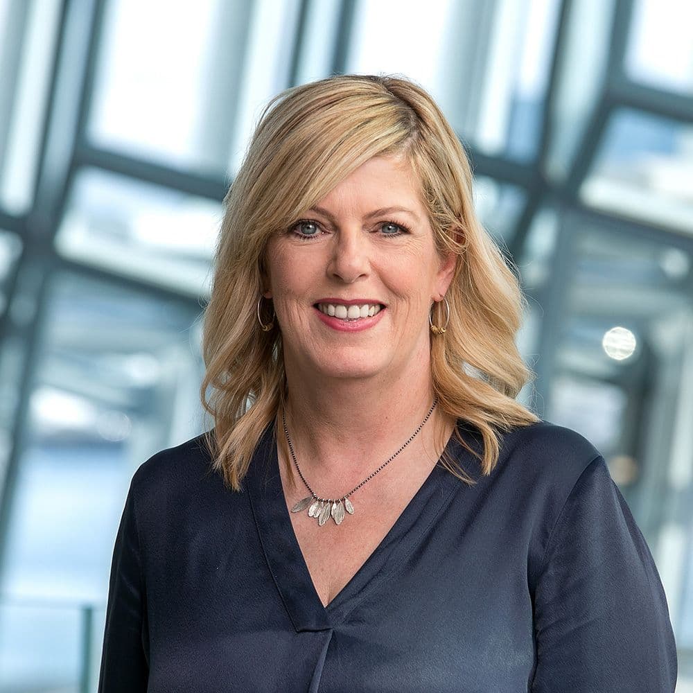 a woman wearing a blue shirt and a necklace is smiling for the camera .