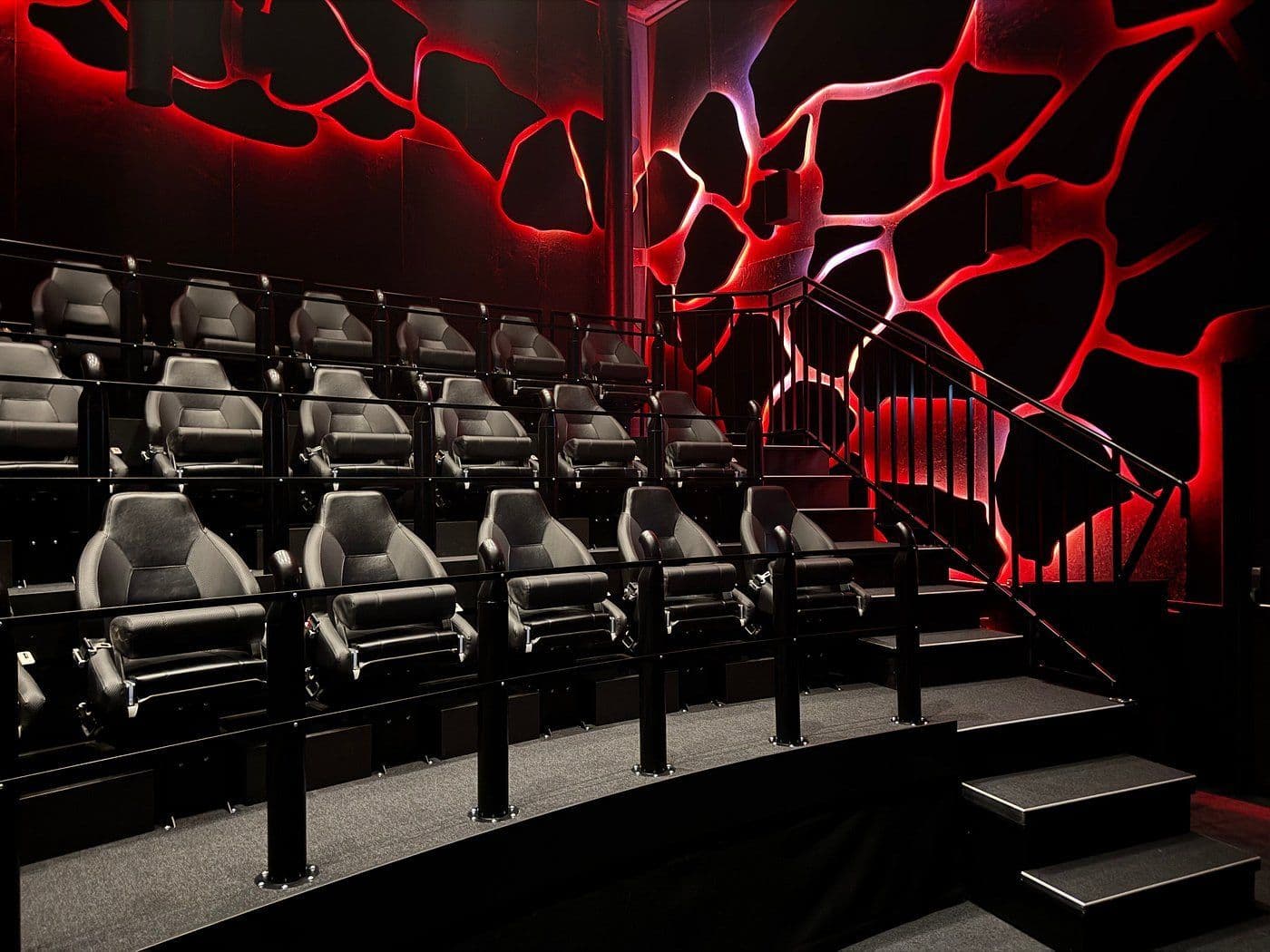 Empty dark grey simulator seats in a dark room with black walls featuring red, abstract LED lighting, and a staircase.