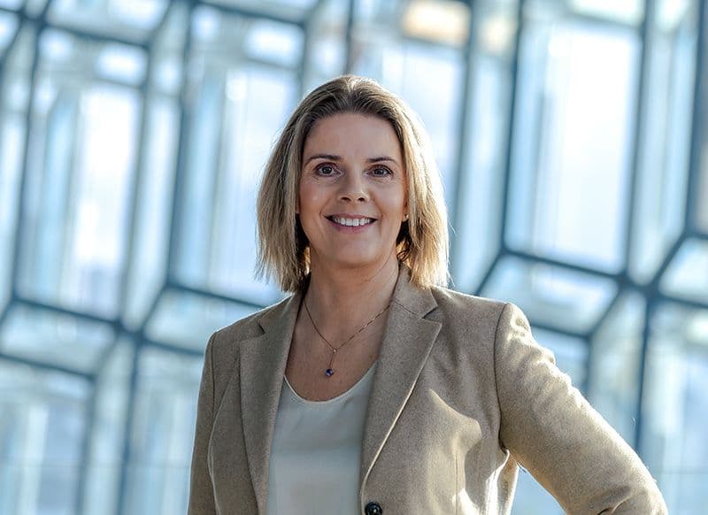 a woman in a tan jacket and white shirt is smiling for the camera .