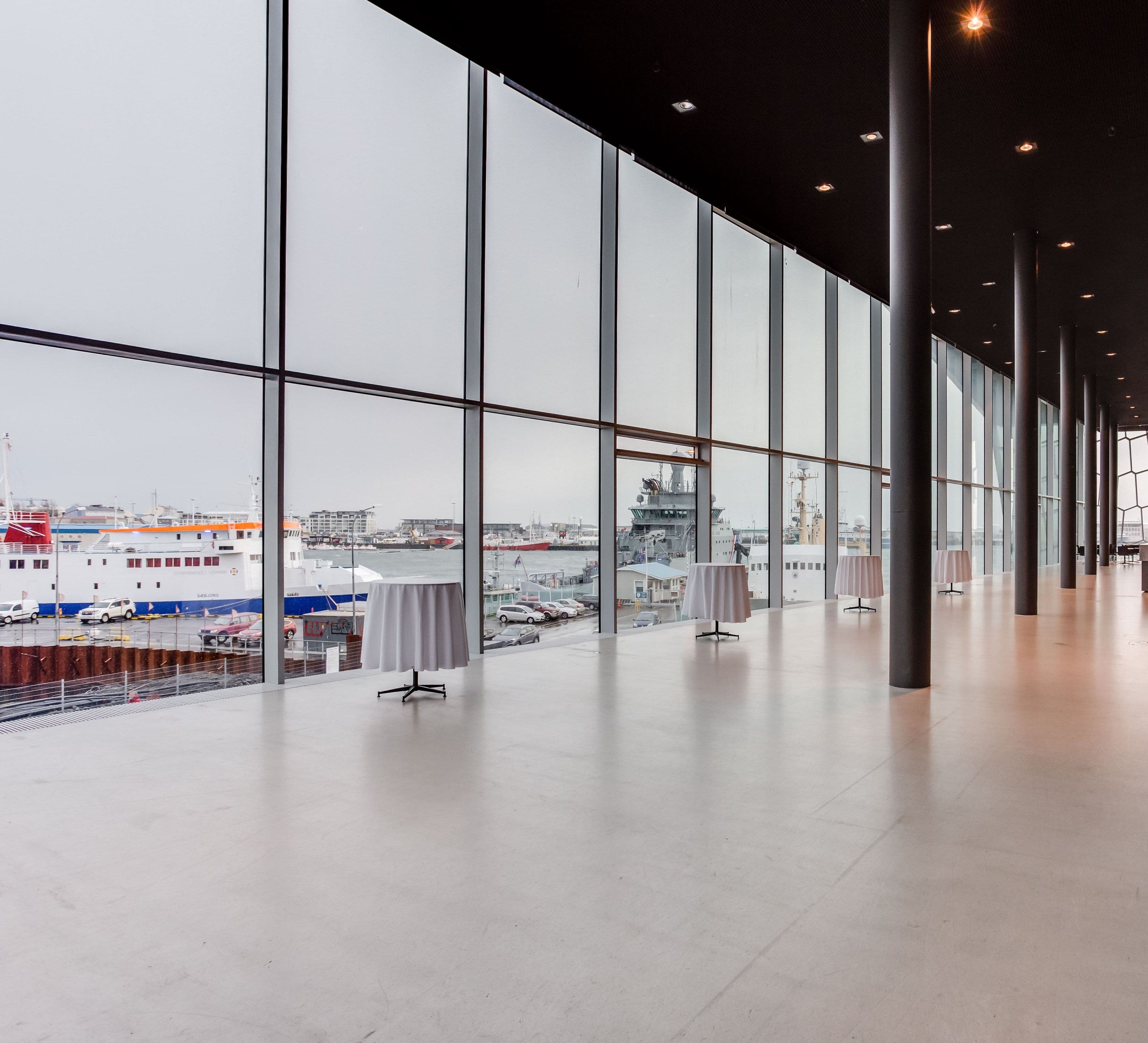 a long hallway in a building with tables and a view of a harbor .