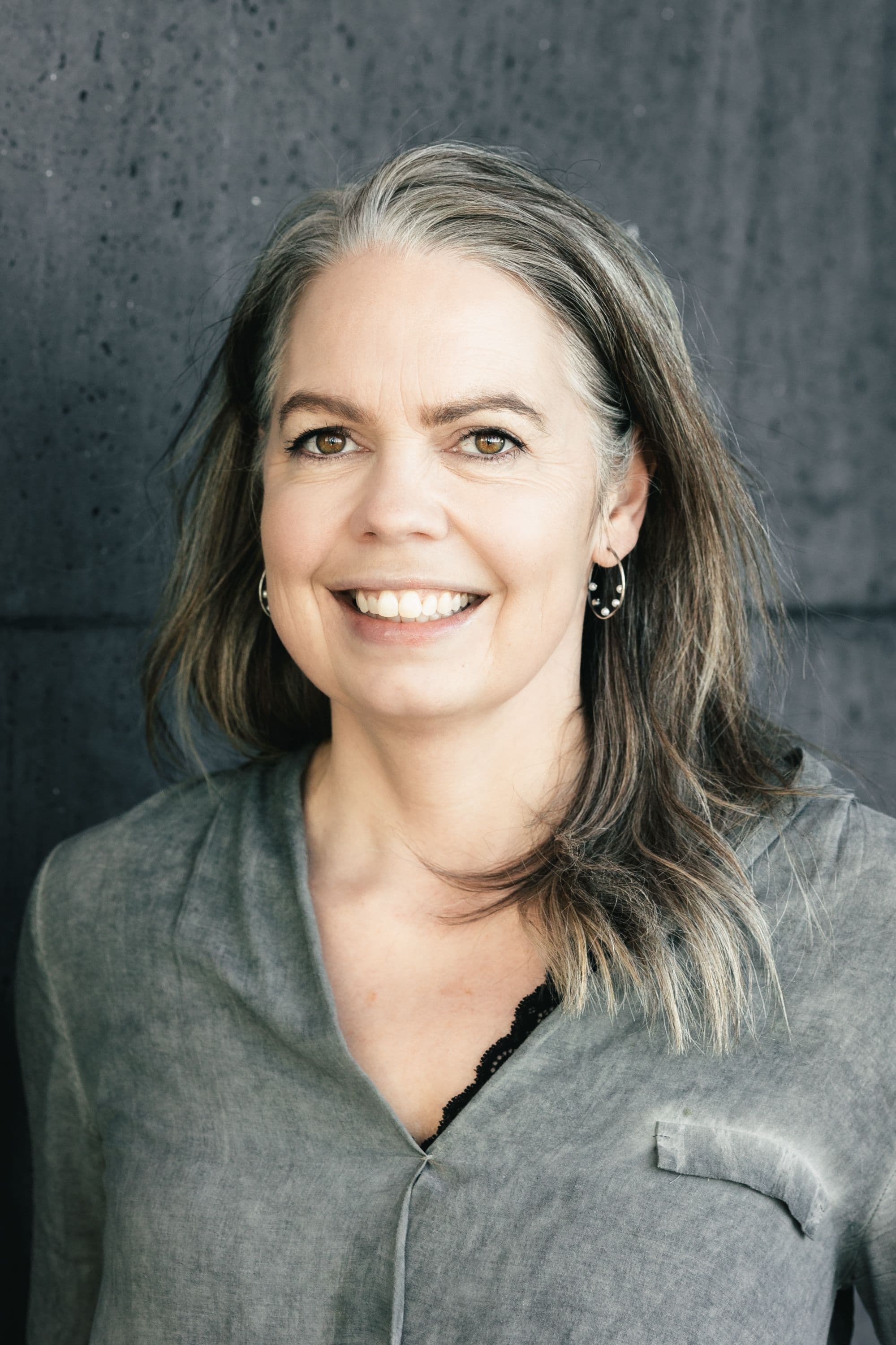 a woman with gray hair and hoop earrings smiles for the camera