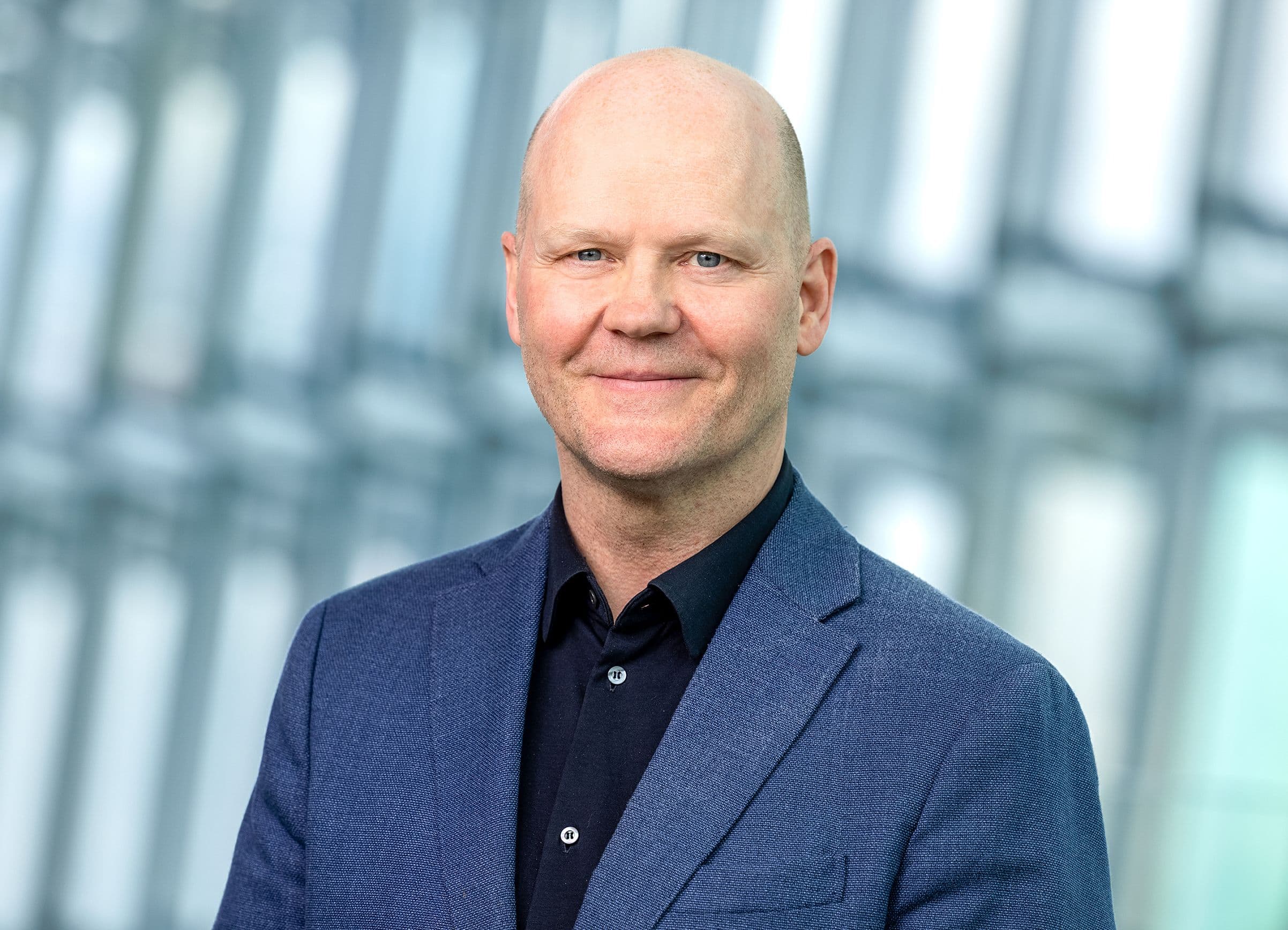 a bald man in a blue suit and black shirt is smiling for the camera .